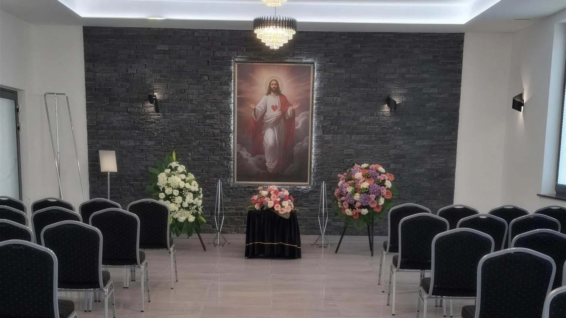 Sala pożegnań w Domu Pogrzebowym Dygas, rzędy krzeseł i kwiaty przed obrazem
